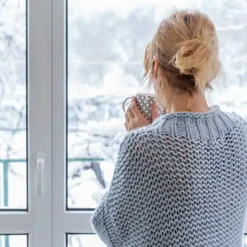 woman drinking coffee looking out winter window
